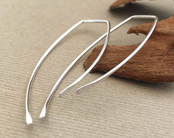 Puede incluir: Un par de pendientes de aro de plata con una forma ligeramente curvada. Los pendientes son simples y elegantes.