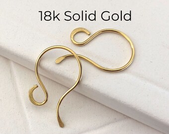 May include: Two 18k solid gold earring hooks. The hooks are made of a smooth, shiny gold metal and are shaped like a teardrop.