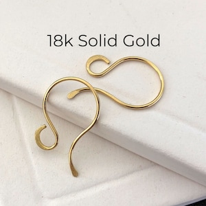 May include: Two 18k solid gold earring hooks. The hooks are made of a smooth, shiny gold metal and are shaped like a teardrop.