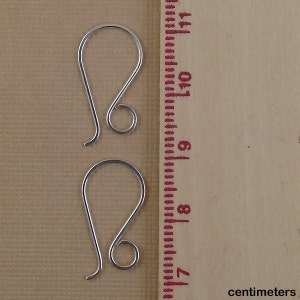 May include: Two silver earring hooks, measuring approximately 1 inch in length, are shown against a brown background with a ruler for scale.