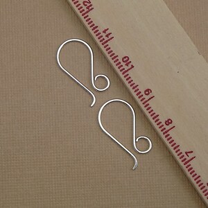 May include: Two silver earring hooks, each measuring approximately 1 inch in length, are shown next to a ruler. The hooks are made of a thin, flexible wire and have a teardrop shape.