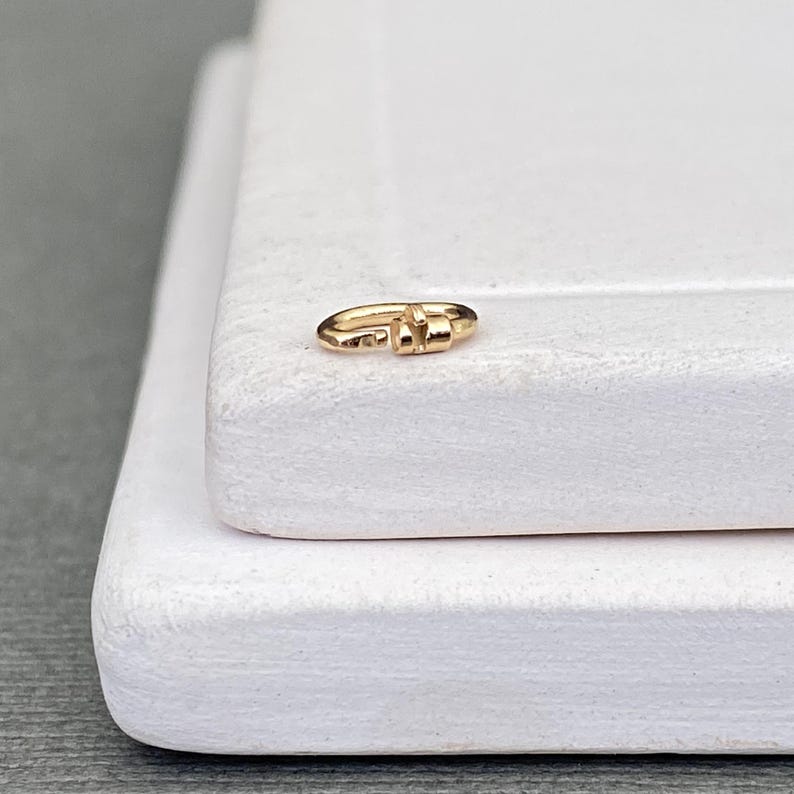 May include: A small, gold-coloured metal jump ring with a visible opening, featuring a polished, reflective surface. The circular jewellery component is designed for connecting chains or charms, showcasing a simple, functional, and metallic construction.