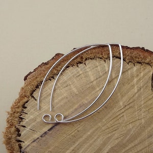May include: Two silver wire earring hoops on a wooden surface. The hoops are oval shaped and have a small loop at the top.