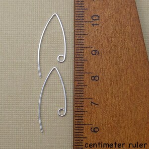 May include: Two silver earring hooks, each measuring approximately 3.5 inches in length, are displayed against a wooden ruler with centimeter markings.