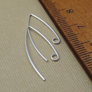 May include: Two silver earring hooks with a rounded loop at the end. The hooks are about 1 inch long and are shown next to a ruler.