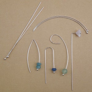 May include: Assortment of silver earring findings with various shapes and beads. The findings include a curved wire, a straight wire, and a wire with a loop at the top. The beads are blue, green, and white.