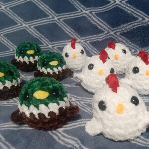 May include: A collection of small, round, crocheted plush figures. Three figures are dark green, white, and brown, resembling mallard ducks with yellow beaks. Four figures are white with red combs and yellow beaks, resembling small chickens.