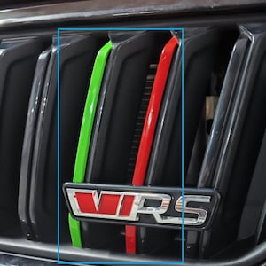 May include: A black car grille with a red, green and white stripe design. The grille has a silver "VRS" emblem.