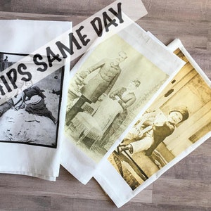 May include: Three white tea towels with black and white vintage photographs printed on them. The photographs show a group of people, a couple, and a person sitting on a bench. The text "Ships Same Day" is printed on the top of the towels.