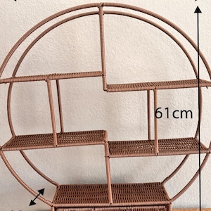 Pode incluir: Uma prateleira de parede redonda castanha com v&aacute;rios n&iacute;veis e uma gaveta. A prateleira tem 55 cm de largura, 61 cm de altura e 10 cm de profundidade. O design apresenta uma textura tecida, adicionando um toque r&uacute;stico &agrave; decora&ccedil;&atilde;o.