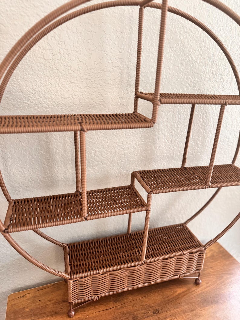 Pode incluir: Uma prateleira de parede redonda marrom com v&aacute;rias prateleiras tecidas e uma base em forma de cesta. A prateleira tem um design em camadas com tamanhos de prateleiras vari&aacute;veis, perfeita para exibir itens pequenos. A estrutura &eacute; feita de um material resistente.