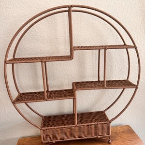 Pode incluir: Uma prateleira marrom, circular, de vime tecido com v&aacute;rios n&iacute;veis. A prateleira tem um design &uacute;nico com uma estrutura semicircular e v&aacute;rias prateleiras retangulares de tamanhos variados. A prateleira foi projetada para ser montada na parede.