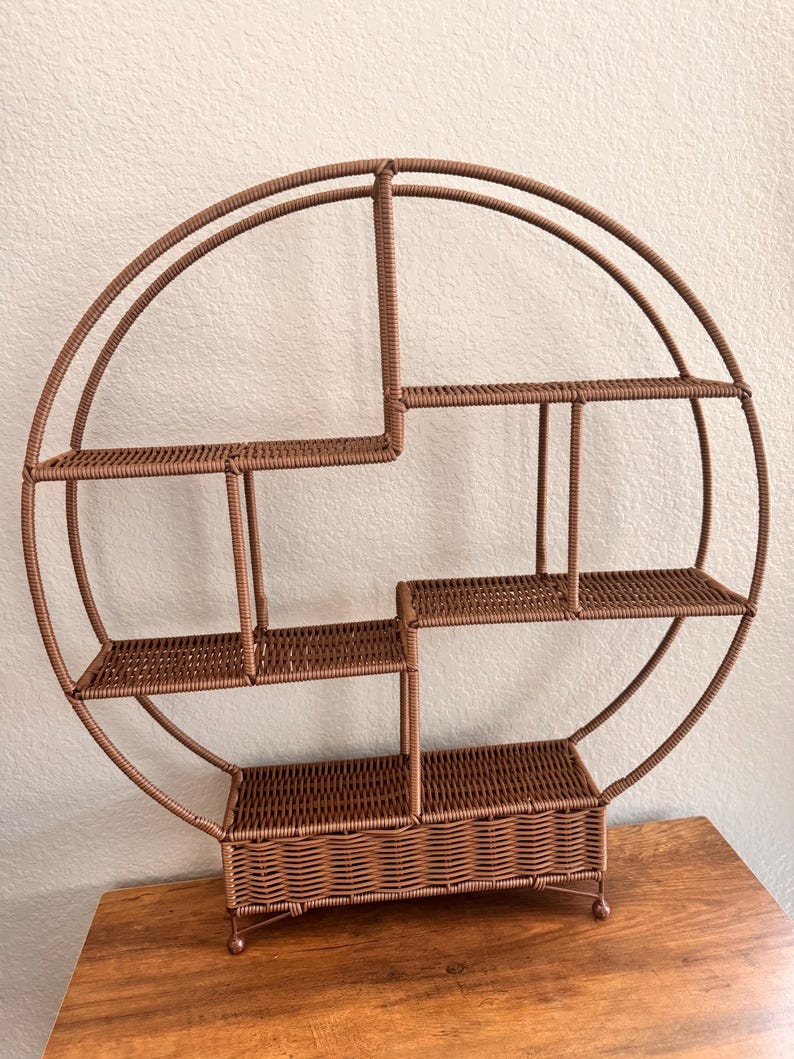 Pode incluir: Uma prateleira marrom, circular, de vime tecido com v&aacute;rios n&iacute;veis. A prateleira tem um design &uacute;nico com uma estrutura semicircular e v&aacute;rias prateleiras retangulares de tamanhos variados. A prateleira foi projetada para ser montada na parede.