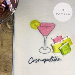 May include: Embroidered design of a pink Cosmopolitan cocktail with a lime wedge on a white towel. The word "Cosmopolitan" is embroidered below the cocktail.  There are four spools of embroidery floss in pink, yellow, and green.
