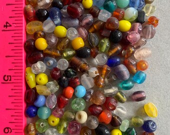 May include: A large assortment of colorful glass beads in various shapes and sizes. The beads are a mix of opaque and transparent colors, including blue, green, red, yellow, and brown.