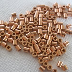 May include: A large pile of copper-colored metal jump rings. The rings are small and round, with a hole in the center. They are perfect for jewelry making.