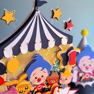 May include: A colorful circus-themed cake topper with a blue and white striped tent, stars, and cartoon characters. The topper includes the name "Noah" and the number "1", perfect for a first birthday celebration.