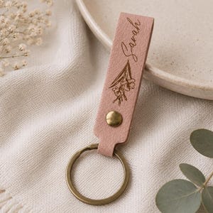 Custom name leather keychain with engraved birth flower and durable metal key ring. The handcrafted leather accessory is beautifully packaged and ready to give as a meaningful personalized gift.