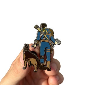 May include: A metal pin featuring a cartoon character wearing a blue jumpsuit and holding a gun, standing next to a brown and black dog. The character has a yellow number "111" on their chest.