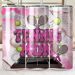 May include: A pink and white tumbler with a tennis theme. The design includes tennis rackets, tennis balls, and the words "TENNIS MOM" in a sparkly pink font. A tennis net and court are also featured.