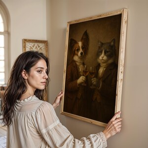 Op de afbeelding: Een ingelijst schilderij in vintage-stijl toont een hond en een kat in formele kleding, elk met een wijnglas. Het kunstwerk heeft een licht houten frame en een sepia-kleurenpalet, wat een klassieke uitstraling cre&euml;ert.