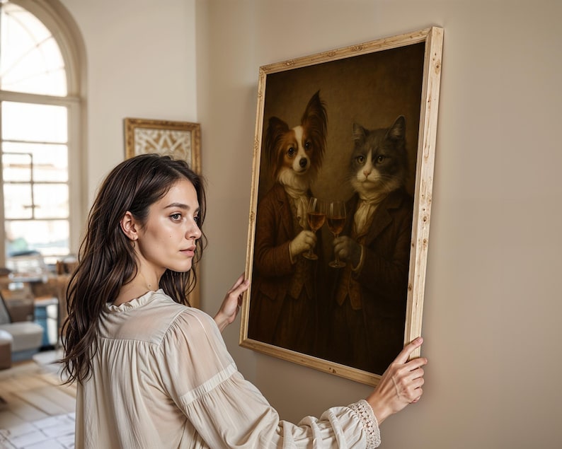 Op de afbeelding: Een ingelijst schilderij in vintage-stijl toont een hond en een kat in formele kleding, elk met een wijnglas. Het kunstwerk heeft een licht houten frame en een sepia-kleurenpalet, wat een klassieke uitstraling cre&euml;ert.