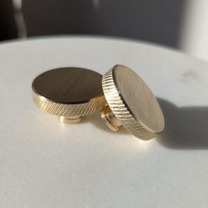 May include: Two gold-colored metal knobs with a ridged edge and a smooth top surface.
