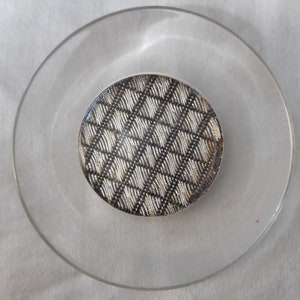 May include: A round, silver-colored button with a black and white geometric pattern.