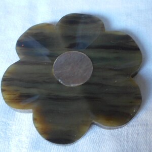 May include: A brown and black flower-shaped coaster with a round, brown, felt-like backing.