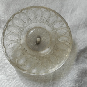 May include: A clear glass button with a decorative, scalloped edge and a smaller, clear button in the center.
