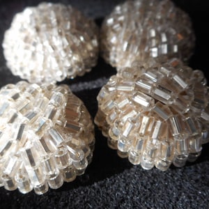 May include: Four round, white, beaded buttons with a shiny, iridescent finish.