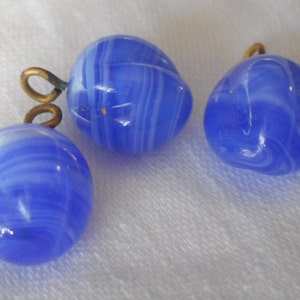 May include: Three blue and white glass beads with gold metal loops. The beads have a swirled pattern.