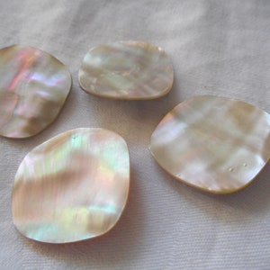 May include: Four iridescent white mother of pearl shell buttons. The buttons are oval shaped and have a smooth, polished surface.