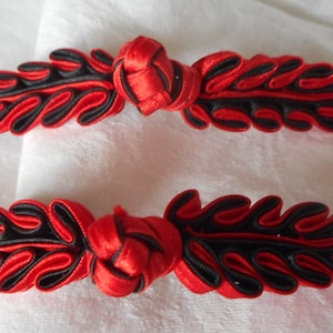 May include: Two red and black Chinese knot buttons with a leaf design. The knots are tied in a traditional style and are made of satin ribbon.