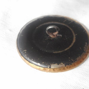 May include: A black button with a gold rim and a metal loop on the top.
