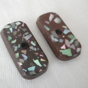 May include: Two brown rectangular buttons with a hole in the center. The buttons are covered in iridescent, multi-colored, speckled pieces of material.
