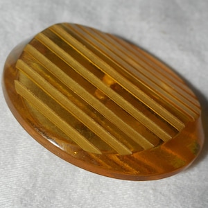 May include: A large, round, amber-colored button with a striped pattern. The button has a raised, textured surface and a smooth, rounded edge.