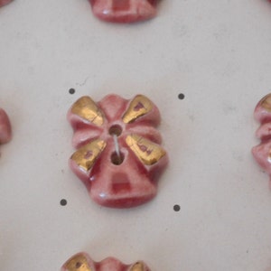 May include: A collection of pink ceramic buttons with gold accents. Each button features a flower-like design with five petals.