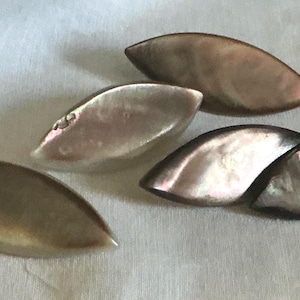 May include: A collection of five marquise-shaped buttons crafted from iridescent mother-of-pearl. Each button features a smooth, curved surface with natural variations in color, ranging from light silver and cream to deep brown and dark gray tones.