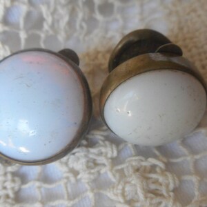 May include: A pair of vintage clip-on earrings with white, round, ceramic stones set in gold-toned metal.
