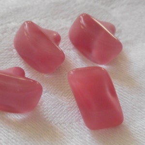 May include: Four pink glass buttons in various shapes. The buttons are smooth and have a glossy finish.