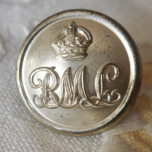 May include: A silver button with a crown and the letters "R.M.C." engraved on it.