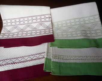 May include: Two white kitchen towels with embroidered borders. One towel has a burgundy border with a geometric pattern in burgundy thread. The other towel has a green border with a geometric pattern in green thread.