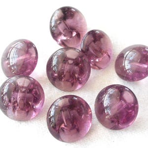May include: Eight round, purple glass buttons with a hole in the center. The buttons are translucent and have a slightly iridescent sheen.