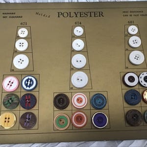 May include: A vintage button card featuring various button designs and sizes. The card is labeled "POLYESTER" and includes text such as "WASHABLE" and "HEAT RESISTANCE." Buttons are white, brown, blue, and multi-colored, with different hole configurations and decorative elements.