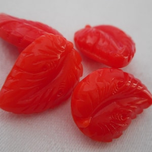 May include: Four bright red glass leaf-shaped beads with a carved design.