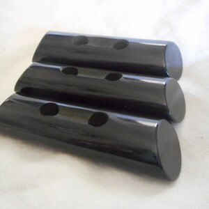 May include: Three black, cylindrical buttons with two holes each. The buttons are stacked on top of each other.