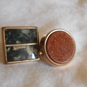 May include: Two cufflinks with a gold-tone finish. One cufflink features a green and white agate stone, the other features a brown sandstone.