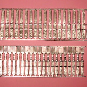 May include: A sheet of metal with 36 silver-colored knives and 36 silver-colored forks. The knives and forks are arranged in rows and are ready to be cut out.