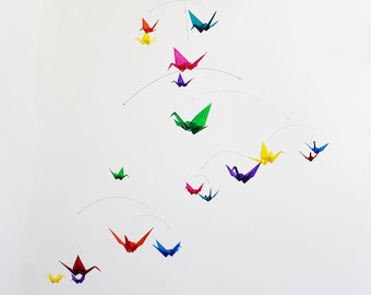May include: A colorful mobile with origami paper cranes in various colors, including red, green, blue, yellow, and purple. The cranes are suspended from a white ceiling.